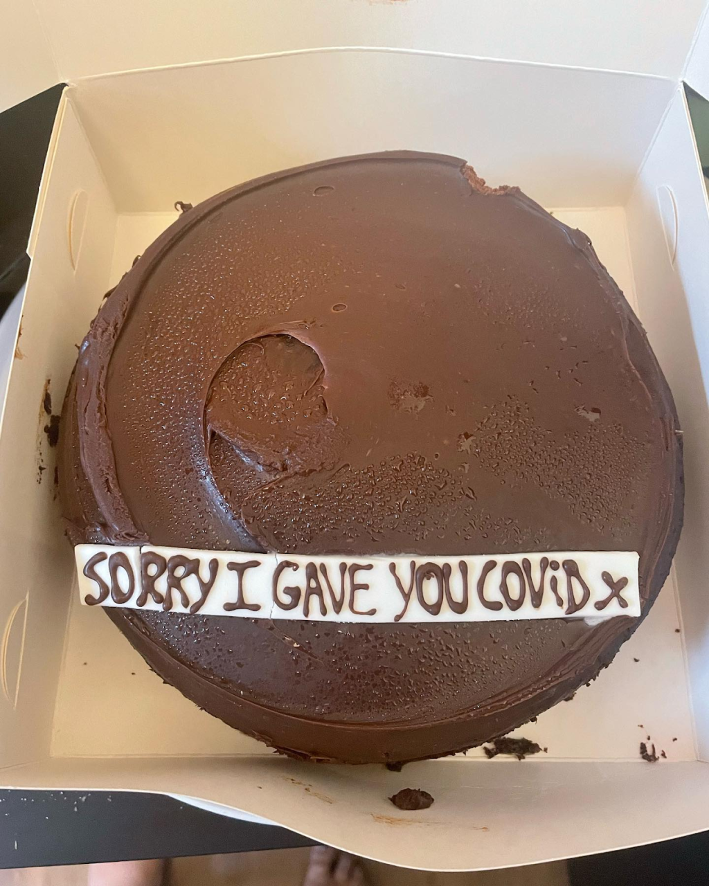 A chocolate cake that says "Sorry I gave you COVID x"